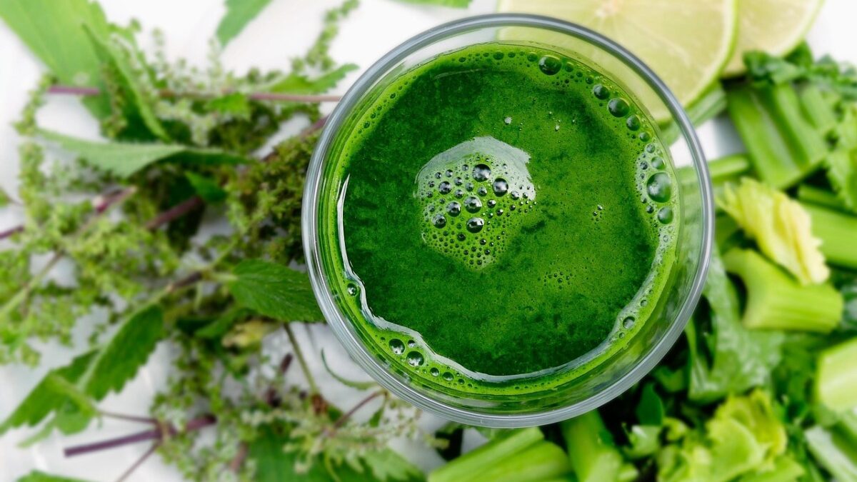 Glas groen sap van bovenaf, omringd door verse kruiden, bleekselderij en limoen