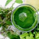 Glas groen sap van bovenaf, omringd door verse kruiden, bleekselderij en limoen